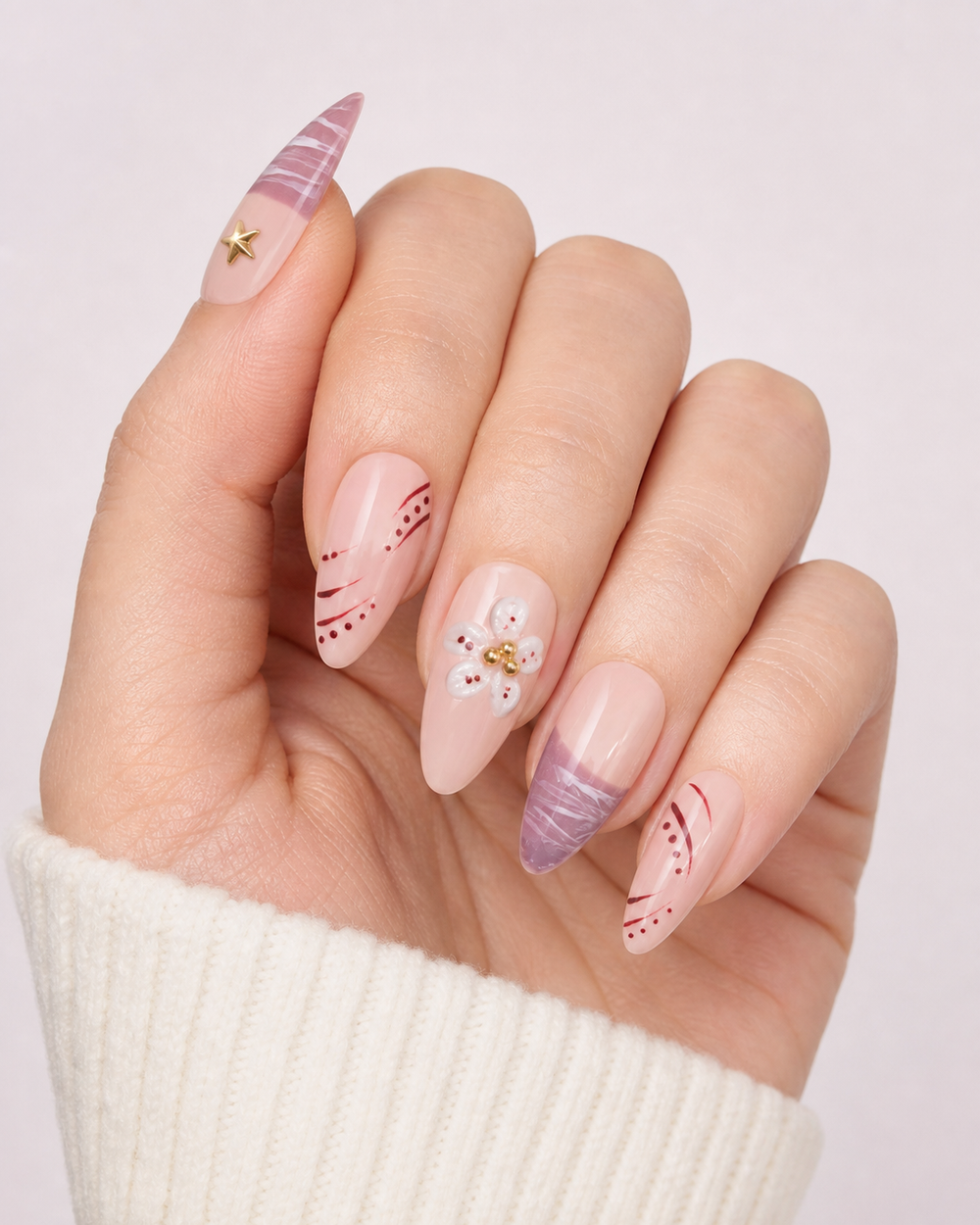 Hand wearing blush and mauve almond press-on nails with floral, star and curved-line details.