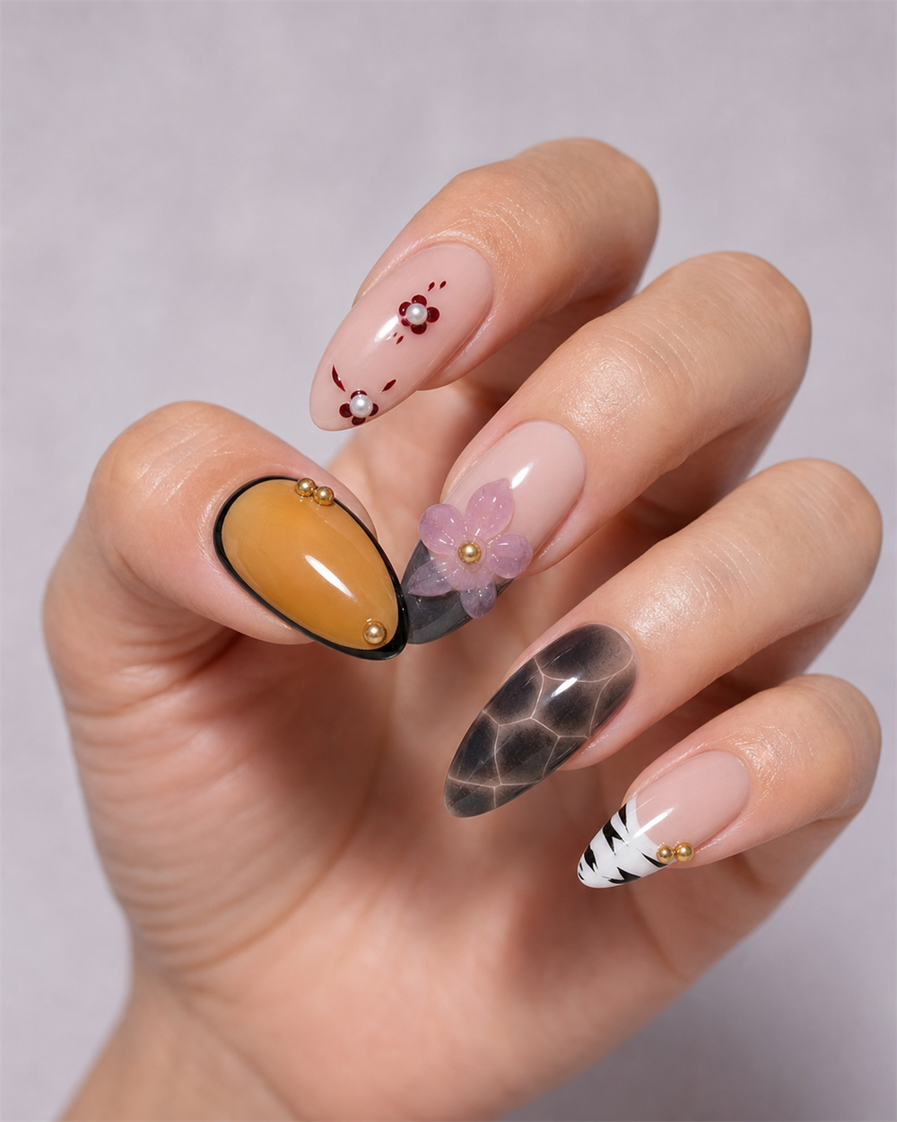 Hand wearing amber, blush and black almond press-on nails with floral and graphic details.